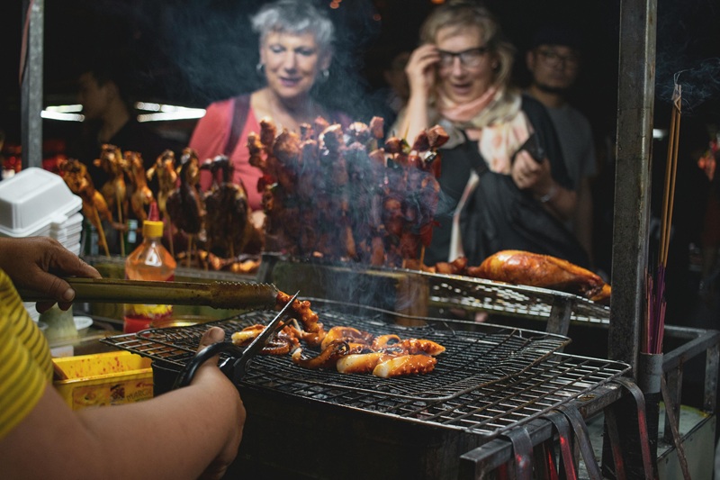 A food festival with people enjoying diverse cuisines, food trucks, and live music under string lights.