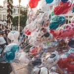 Colorful Disney character balloons on Main Street with a balloon vendor and visitors enjoying the park