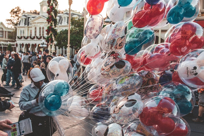 Colorful Disney character balloons on Main Street with a balloon vendor and visitors enjoying the park