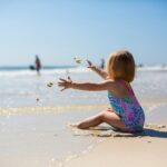 Toddler in colorful swimsuit playing with sand at a sunny Orlando beach