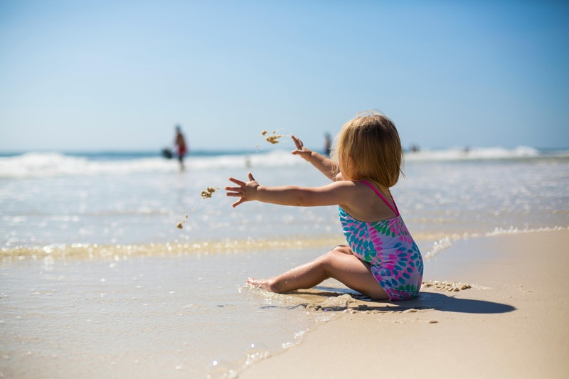 Toddler in colorful swimsuit playing with sand at a sunny Orlando beach