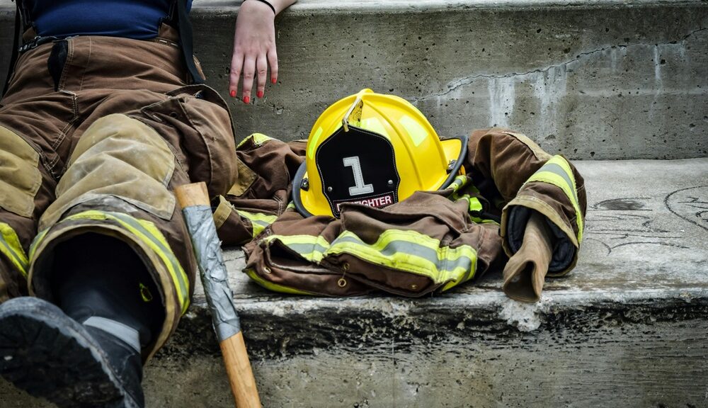 Firefighter resting on concrete steps with gear and helmet beside them