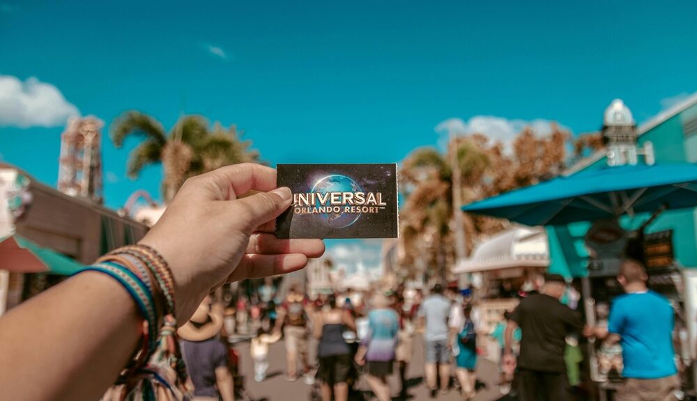 Hand holding a Universal Orlando Resort ticket with theme park crowd in background