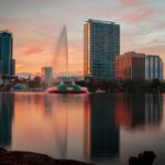 Sunset view of Lake Eola Fountain and downtown Orlando skyline reflected on the water, capturing the city’s cultural and historical essence.