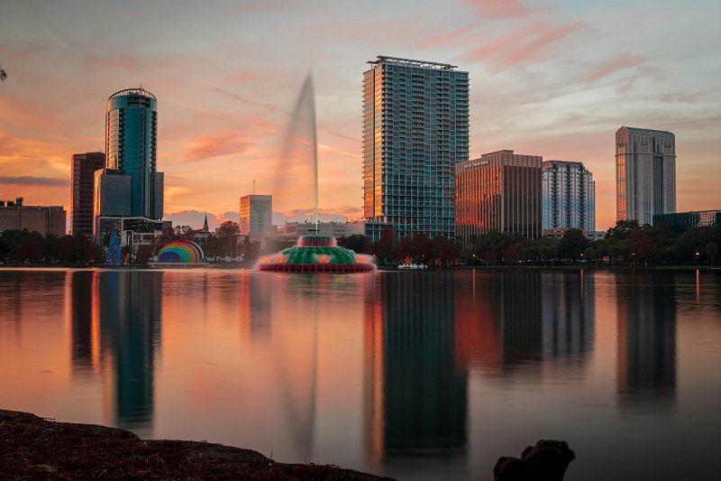 Sunset view of Lake Eola Fountain and downtown Orlando skyline reflected on the water, capturing the city’s cultural and historical essence.