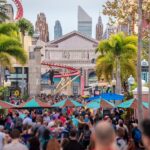 Crowds walking through an Orlando theme park entertainment area lined with palm trees and attractions.
