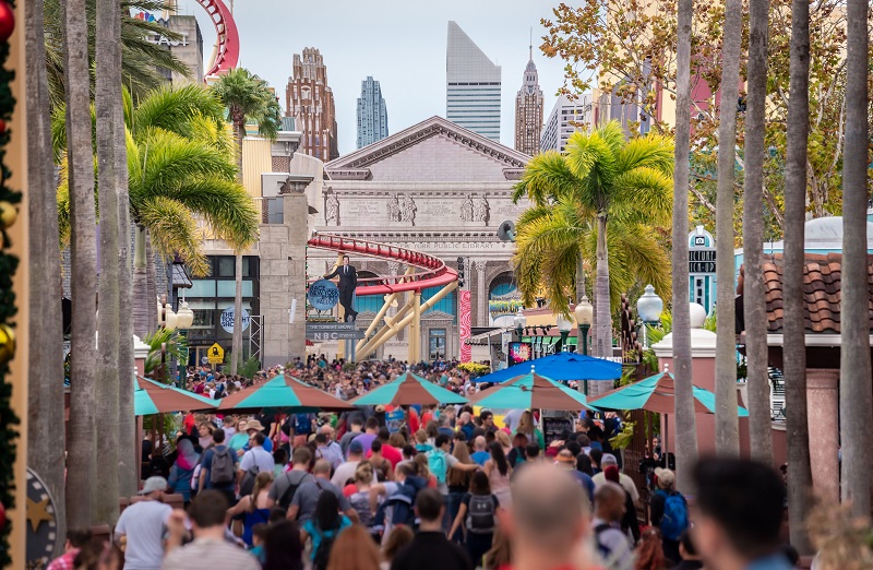 Crowds walking through an Orlando theme park entertainment area lined with palm trees and attractions.